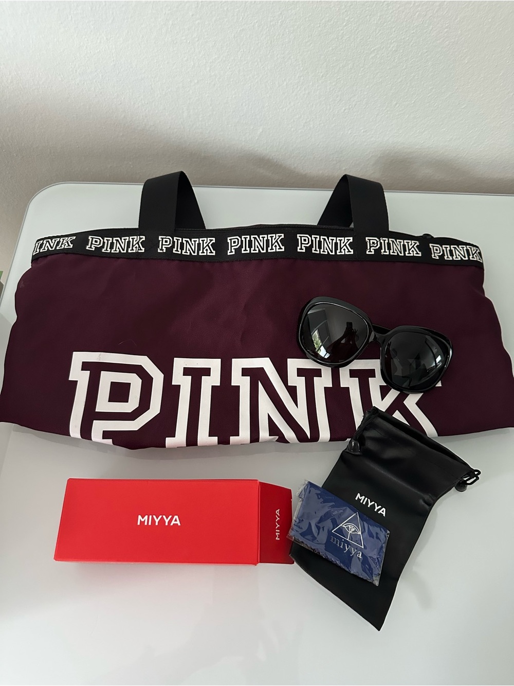 Pink burgundy tote bag and black Miyya sunglasses.